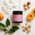 Pūraka Active Day Cream jar with jasmine and neroli flowers on blush stone surface
