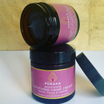 Pūraka Brightening Soothing Hand Cream with Vetiver, Orange and Lavender stacked with the Activated Charcoal Deep Cleansing Mask in amber glass jars against a gold background