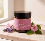 Pūraka Hydrating Face Scrub jar with geranium flowers and lavender on blush stone