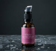 Pūraka Hydrating Super Serum in amber glass pump bottle on wet dark marble surface